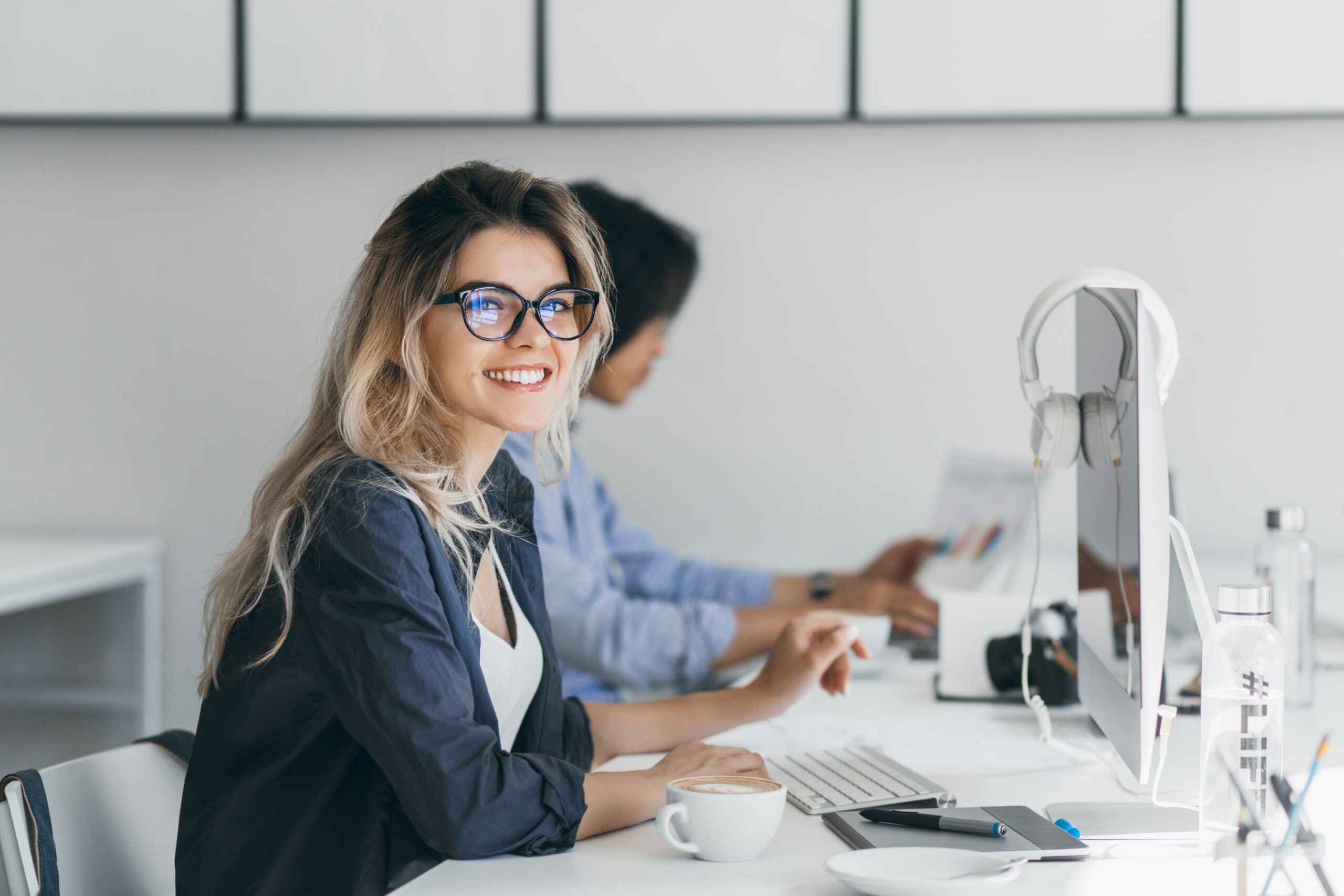 attractive-laughing-freelancer-woman-posing-with-cup-coffee-her-workplace-chinese-student-blue-shirt-works-with-document-campus-with-blonde-friend-glasses-min